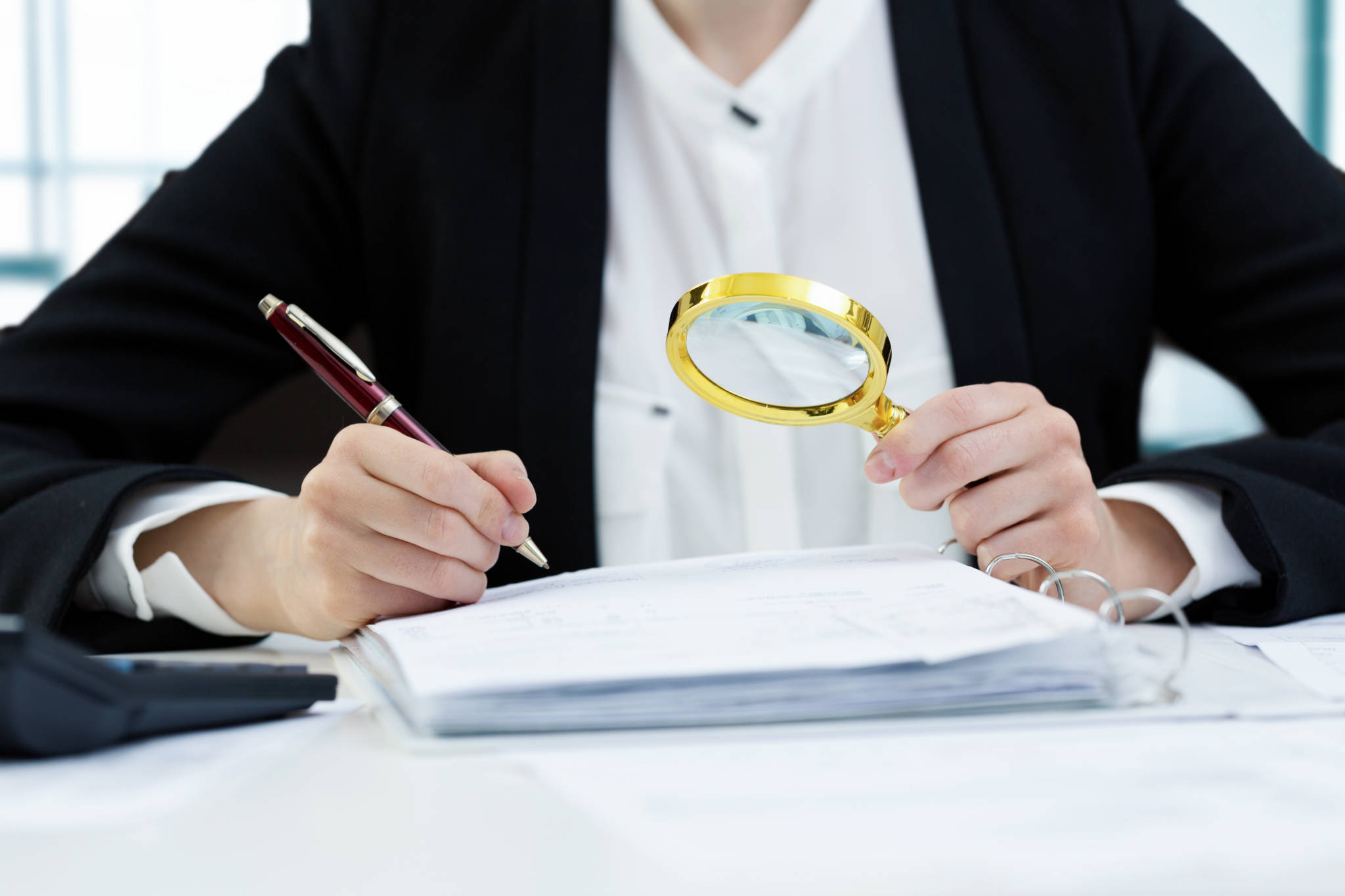 internal audit concept - woman with magnifying glass inspecting documents